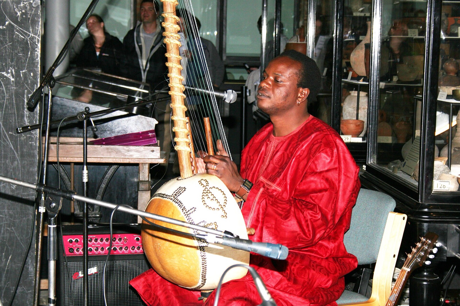 Un músico vestido de rojo toca la kora sobre un escenario.