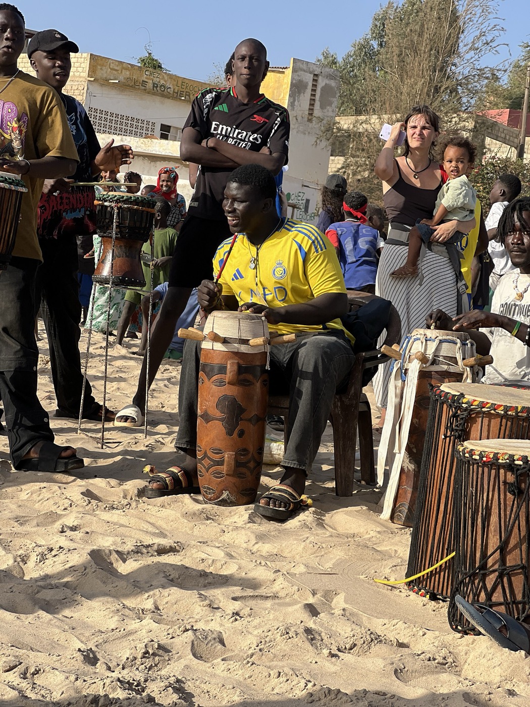 Percusionistas tocan tambores sabar al aire libre, rodeados de gente.